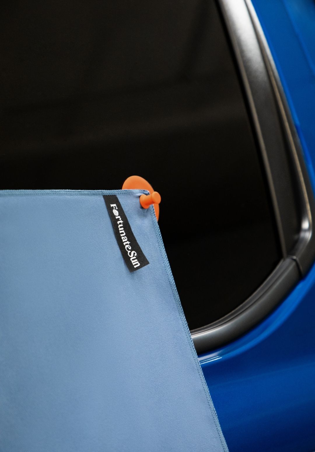 Blue car with Fortunate Sun Hidey towel being stuck to car window using the Hidey suction cups.