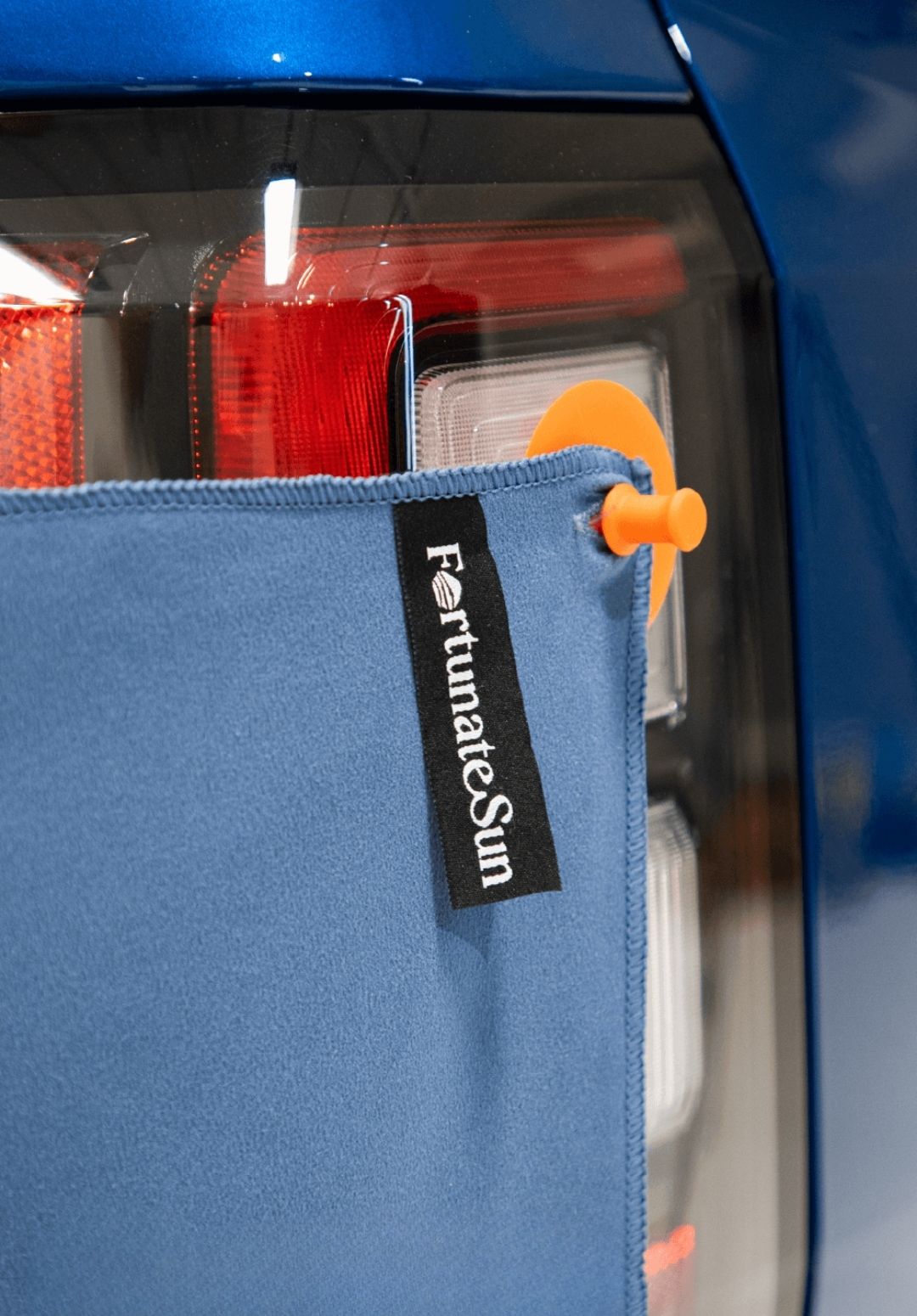 Blue car with Fortunate Sun Hidey towel being hung up by suction cups onto the  cars light.