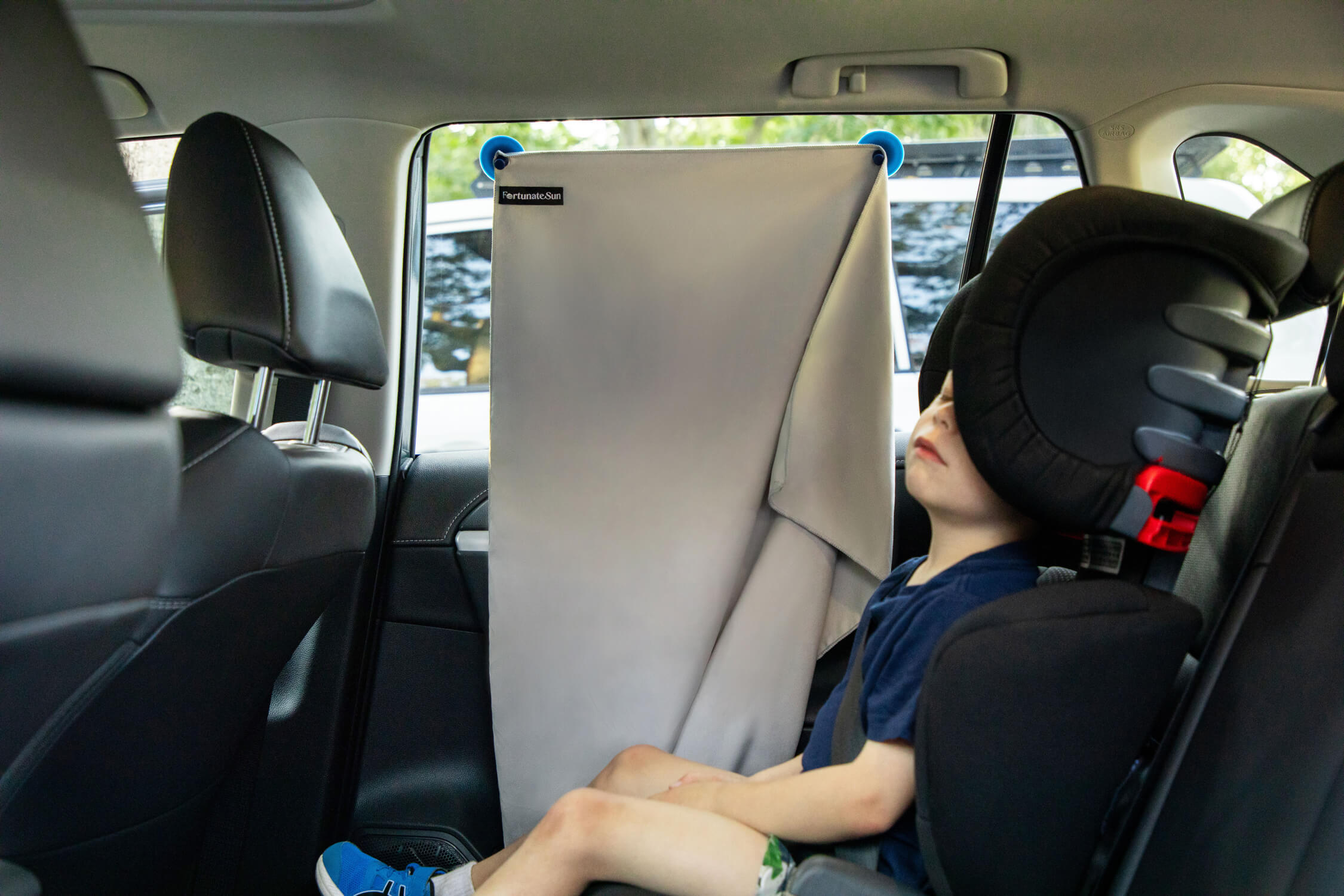 Kid asleep in car with the Fortunate Sun Hidey towel hung on the window to act as a sun shade.
