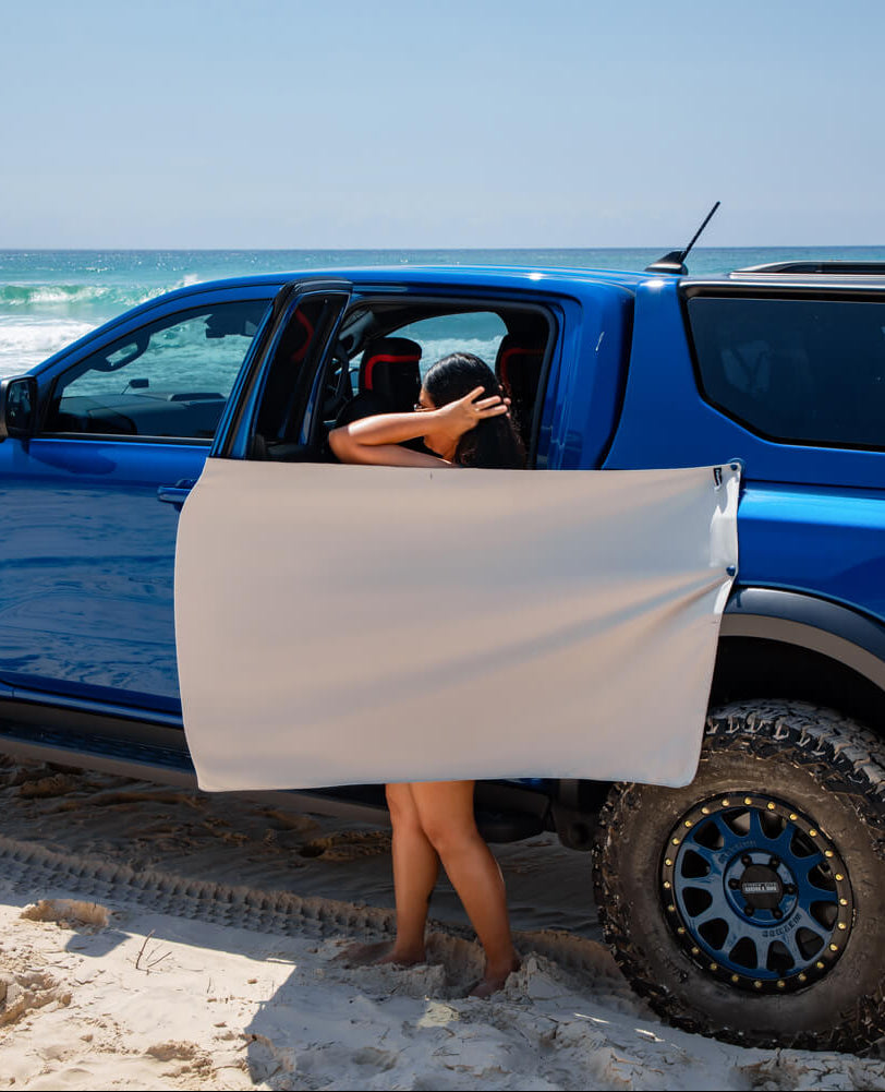 Women using Fortunate Sun magnet towel  as a privacy screen on a blue ute at an Australian beach.